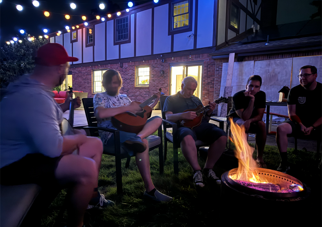 Chris Coyier, Brad Frost, Jeremy Keith playing music while Ian Frost and Josh Sager look on around a camp fire.